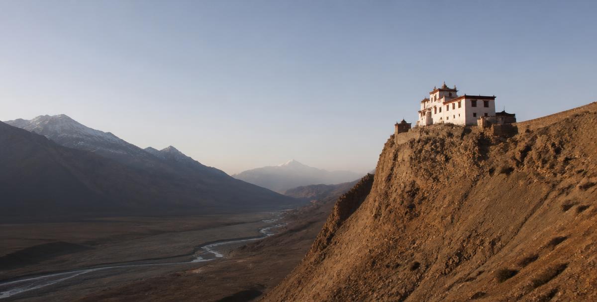 A white Himalayan monastery perched on a stark cliff overlooking a wide valley